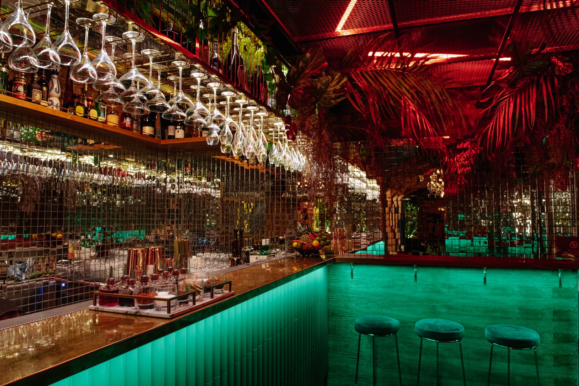 Mirrored bar with hanging glassware under red and emerald light at Cache Cache