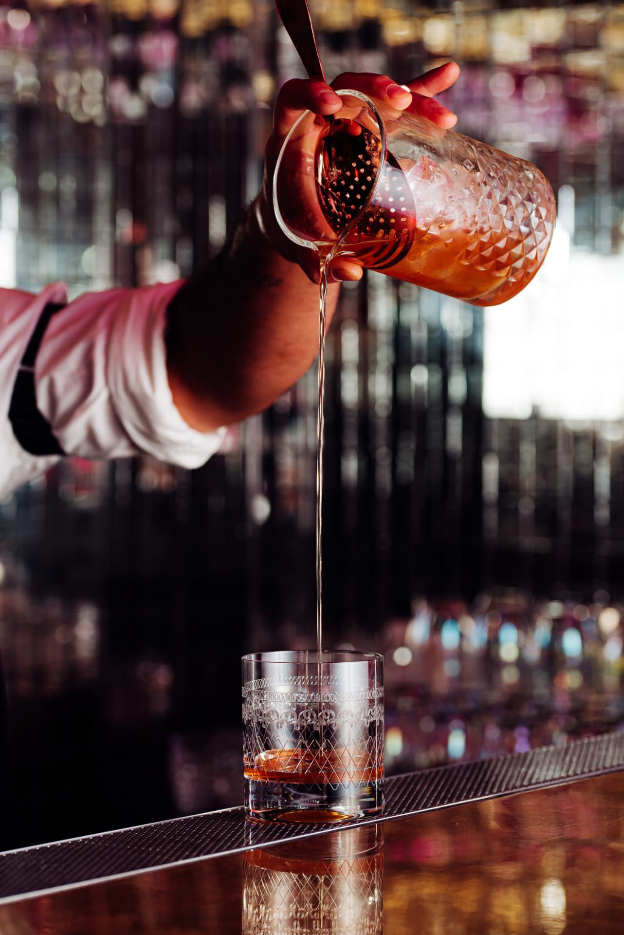 A bartender straining a cocktail into an etched crystal glass at the Cache Cache bar